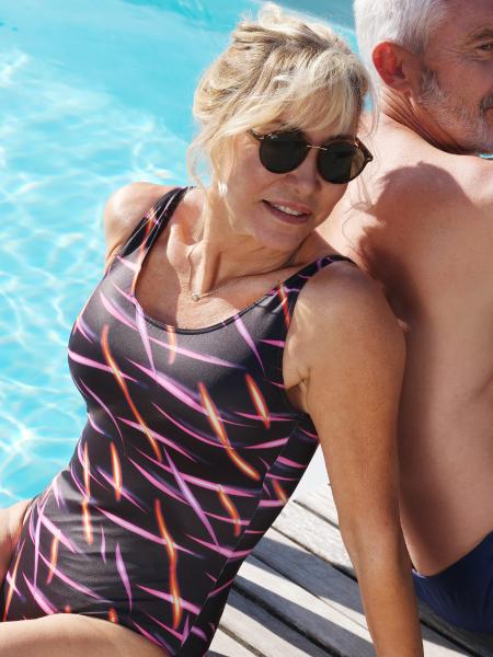 femme en maillot de bain noir imprimé multicolore addossé à un homme au bord de la piscine